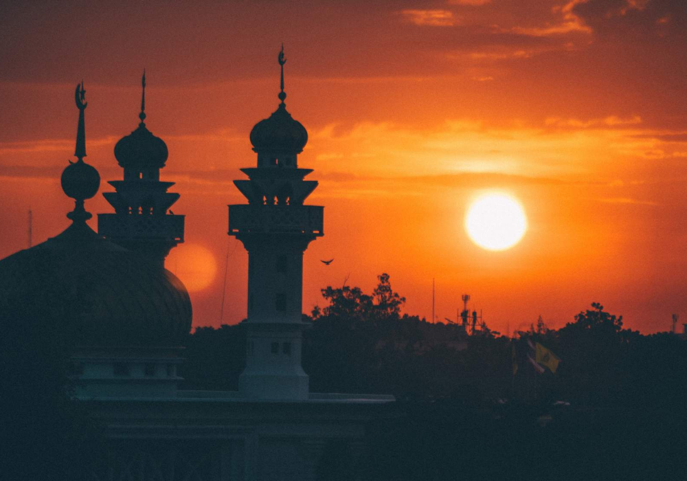 Sunset behind a mosque with silhouettes of minarets and domes.