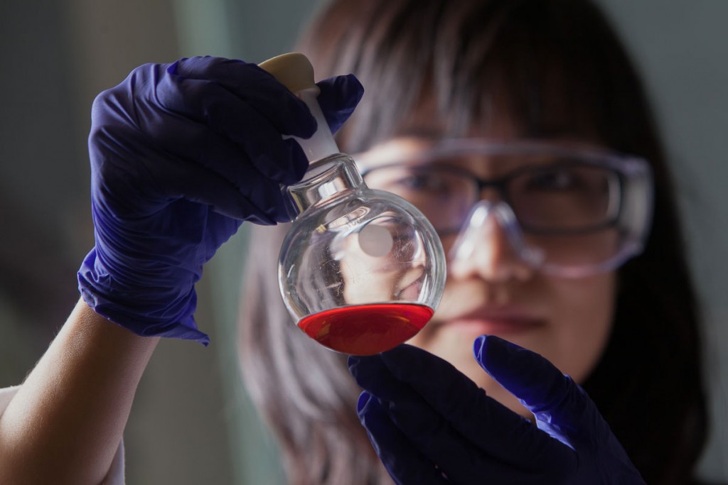 woman wearing googles & gloves looking at a chemical-filled beaker