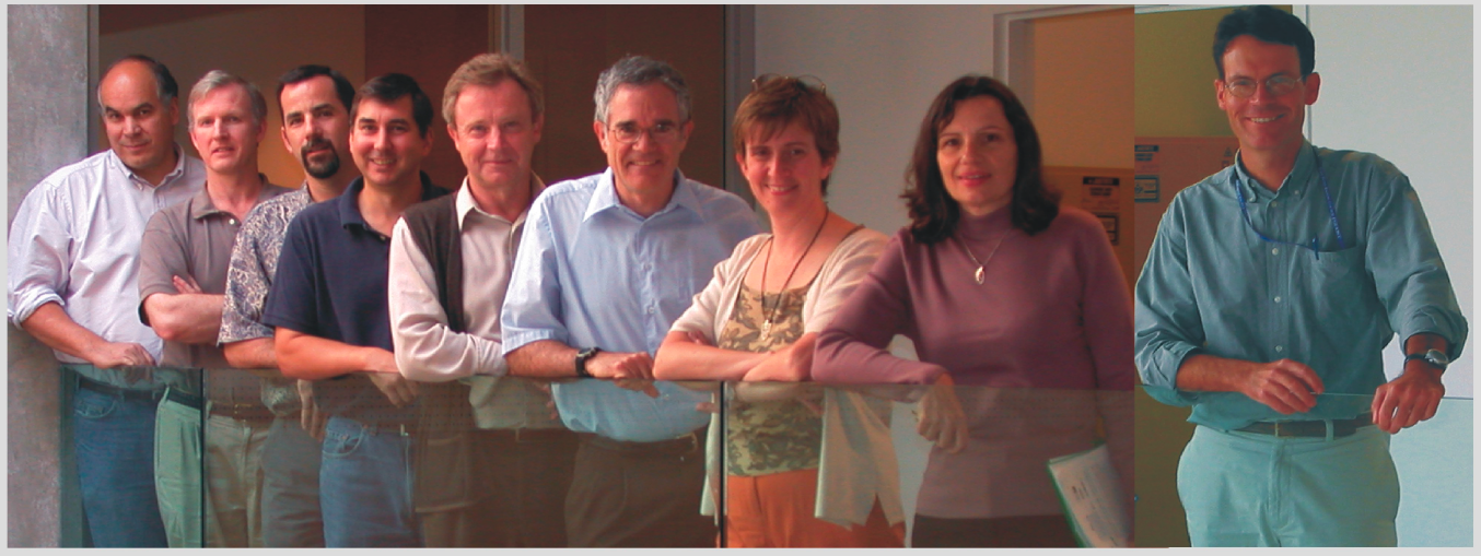 Nine people pose along an indoor glass railing.