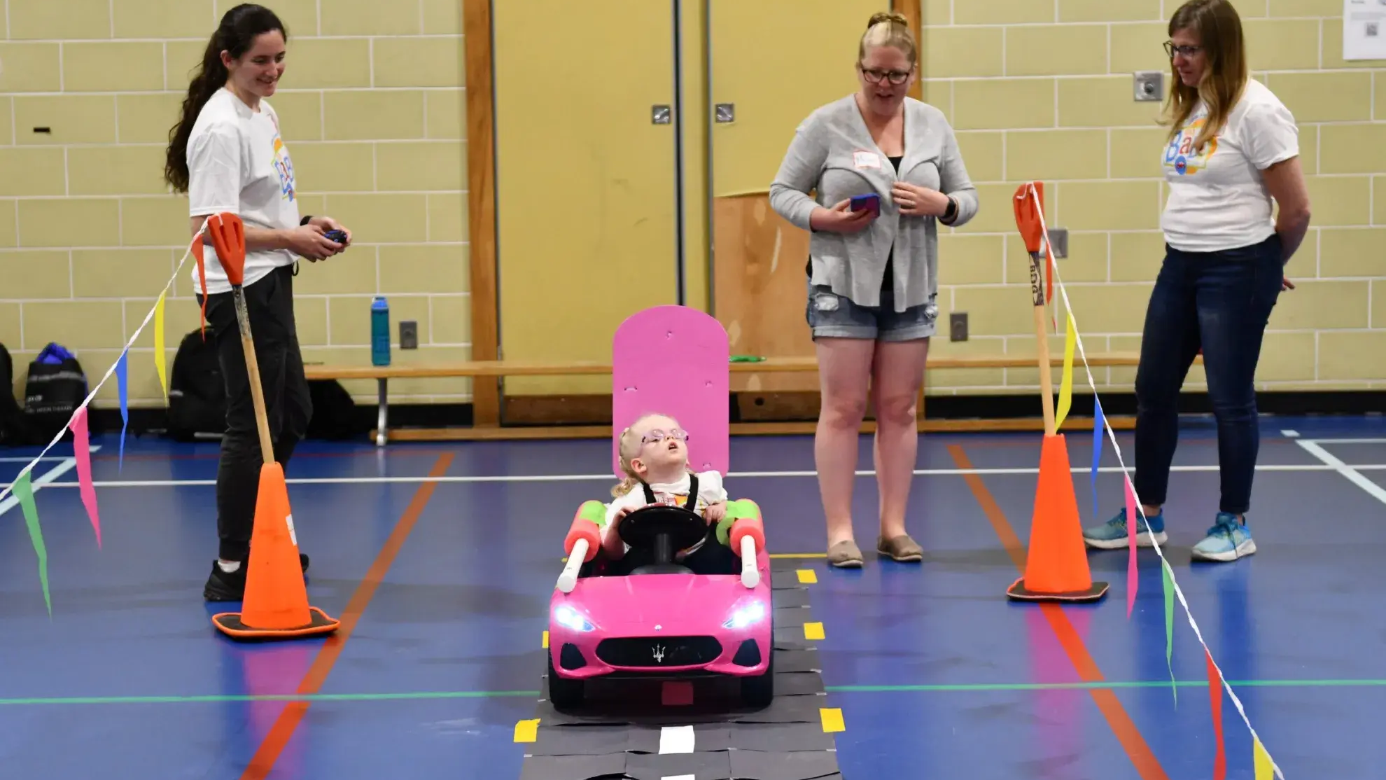 A little girl rides in a pink toy car on a pretend road