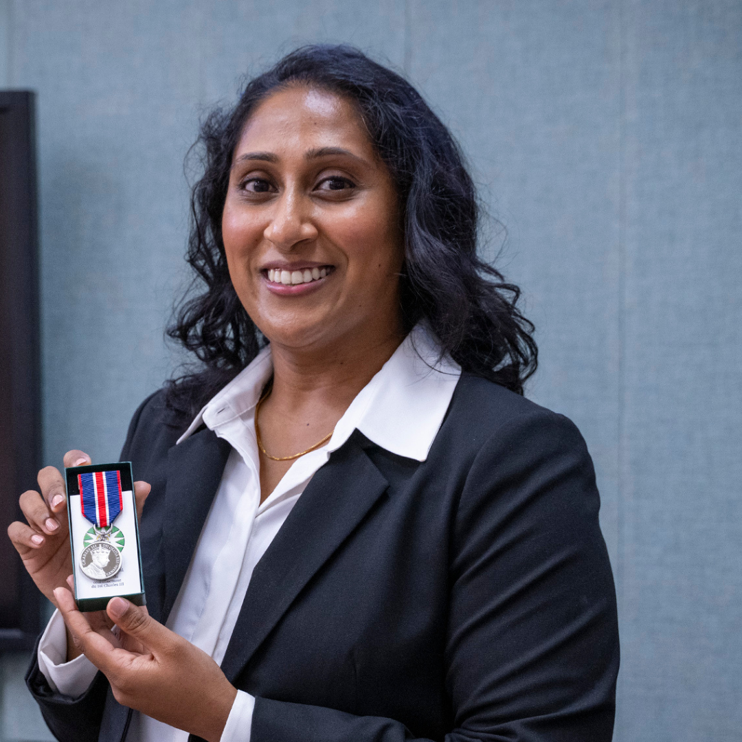 headshot of Dr. Shaira Wignarajah, smiling at the camera as she holds up her King Charles Coronation Medal