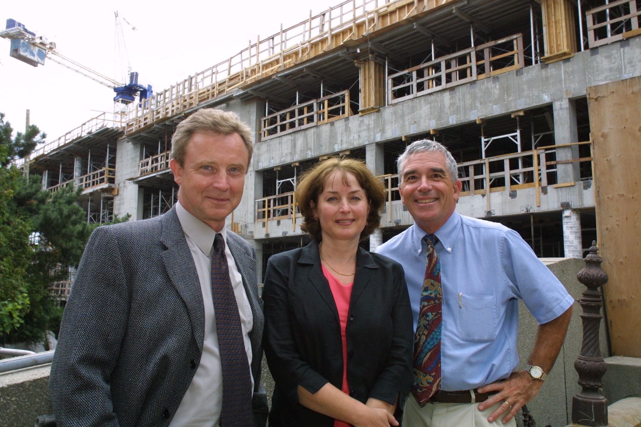  Dr. Roger Deeley, Dr. Elizabeth Eisenhauer and Dr. Joe Pater stand side by side outside the partially constructed Queen’s Cancer Research Institute building, with the unfinished exterior and construction work visible behind them.