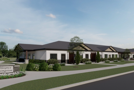 Architectural rendering of Hospice Kingston facility featuring a single-story white sided building with multiple entrances and a landscaped front yard with a sign displaying 'Hospice Kingston.'