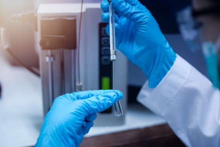 gloved hands handling scientific test tubes and vials in a lab setting