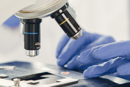 close up shot of microscope with two gloved hands handling a slide
