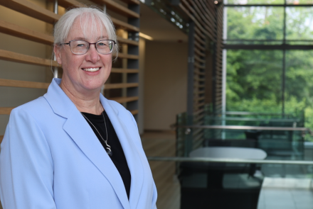 headshot of Dr. Lisa Tannock smiling at the camera wearing a black blouse underneath a baby blue coloured blazer. Her white hair is tied back and she is wearing thin-rimmed glasses