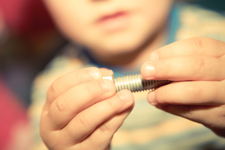 child's hands working with a large screw and bolt to put together