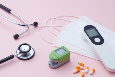 stethoscope, oxygen monitor, medical mask, pills, and health monitor displayed on a flat surface