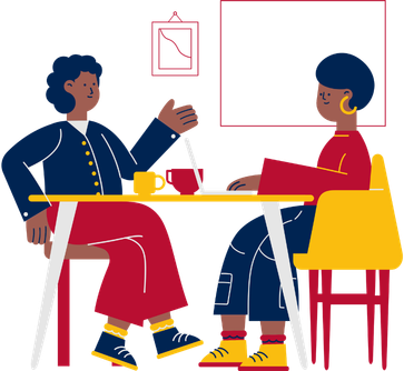 Two people sitting at a table with a laptop between them, appearing to have a conversation.